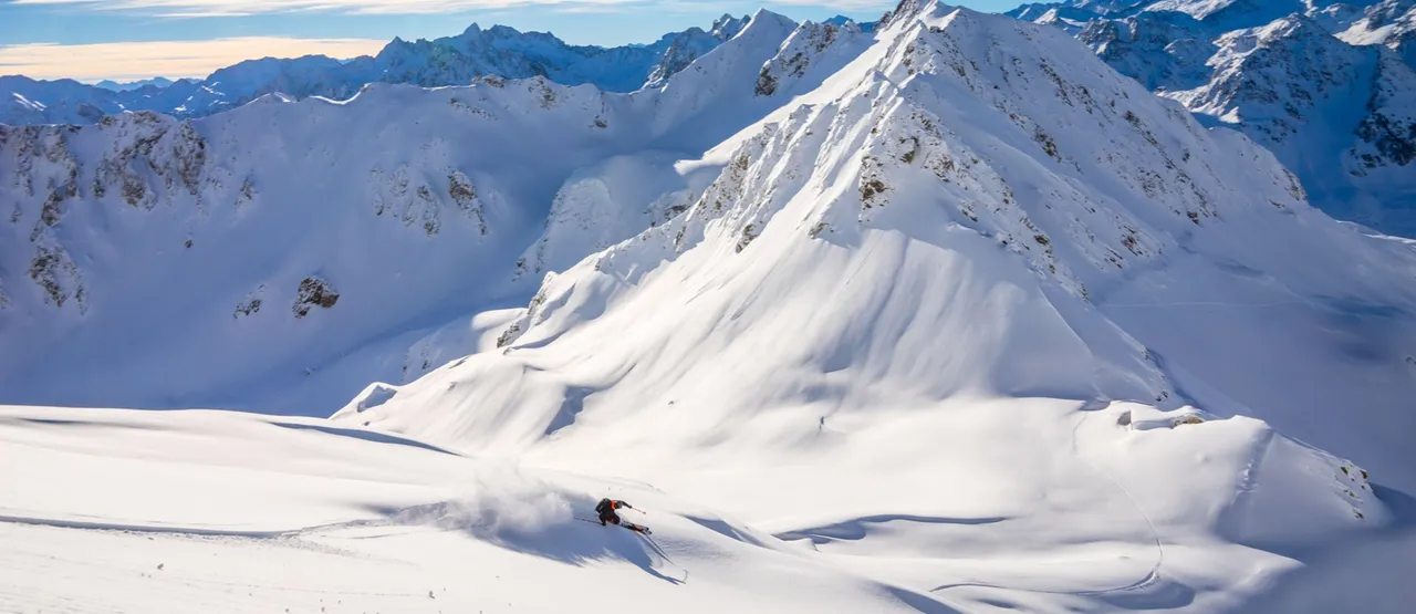 Skier descending through fresh powder with alpine peaks in the background