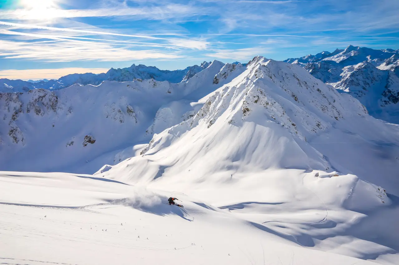 Skier descending a wide snowy slope below an alpine peak