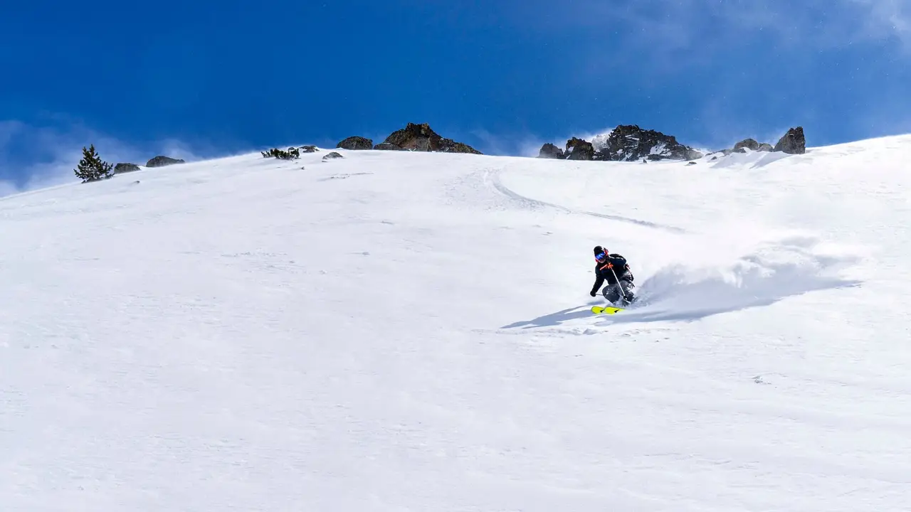 Skier making a powder turn off-piste under a blue sky