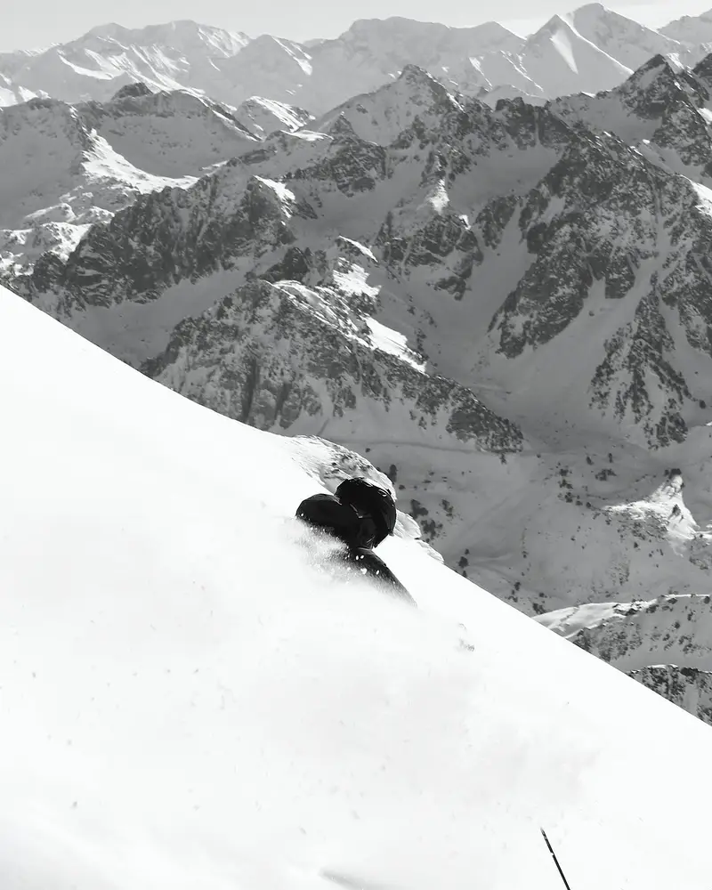 Black and white photo of a skier in deep powder below rocky peaks