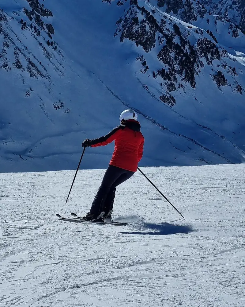 Skier in a red jacket carving on a groomed piste