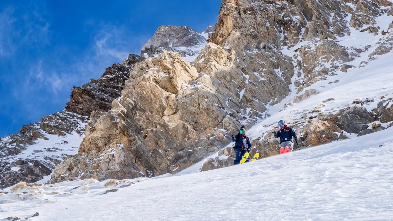Two skiers descending below golden rock faces