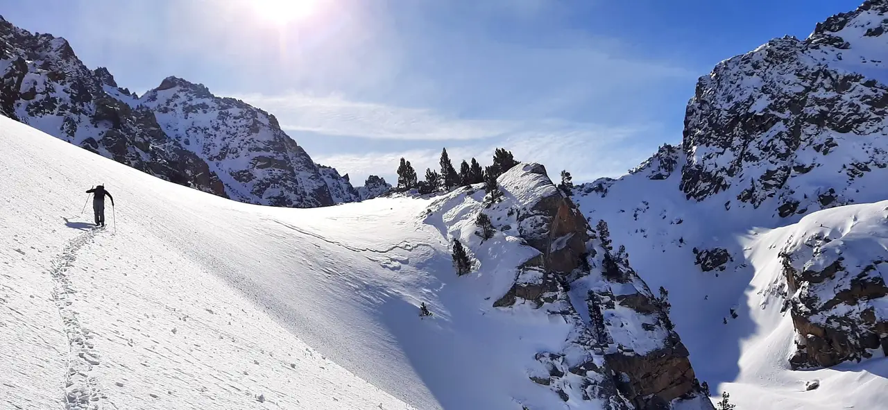 Ski tourer climbing a snowy slope between rocky peaks